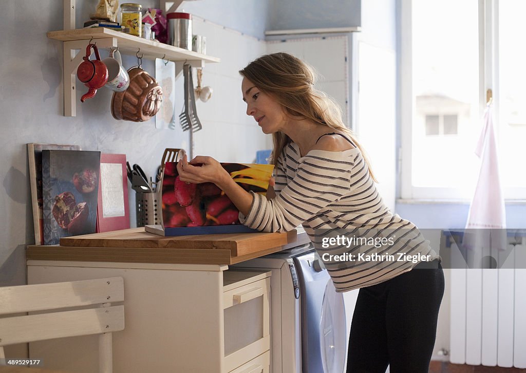 Woman leaning on kitchen counter, reading cookbook