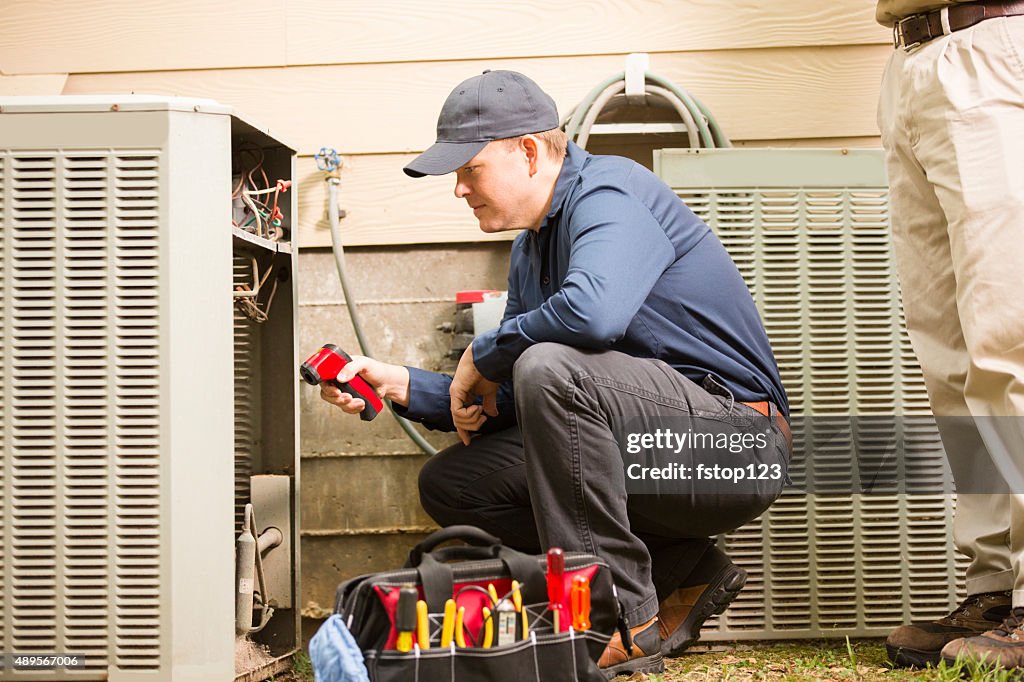 Air conditioner repairmen work on home unit. Blue collar workers.