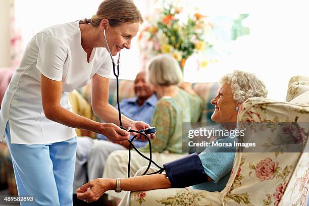 caretaker taking senior woman's blood pressure - curador imagens e fotografias de stock