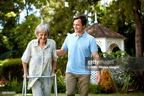 caretaker assisting senior woman in using walker - orthopaedic equipment stock-fotos und bilder