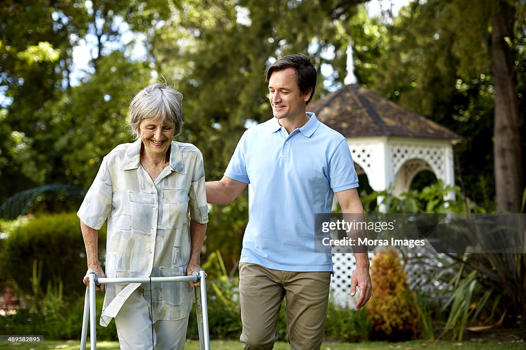 Caretaker assisting senior woman in using walker
