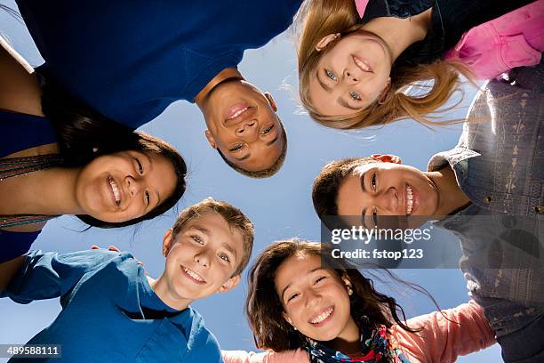 teenagers: diverse group of friends huddle outside together. blue sky. - pre adolescent child stock pictures, royalty-free photos & images