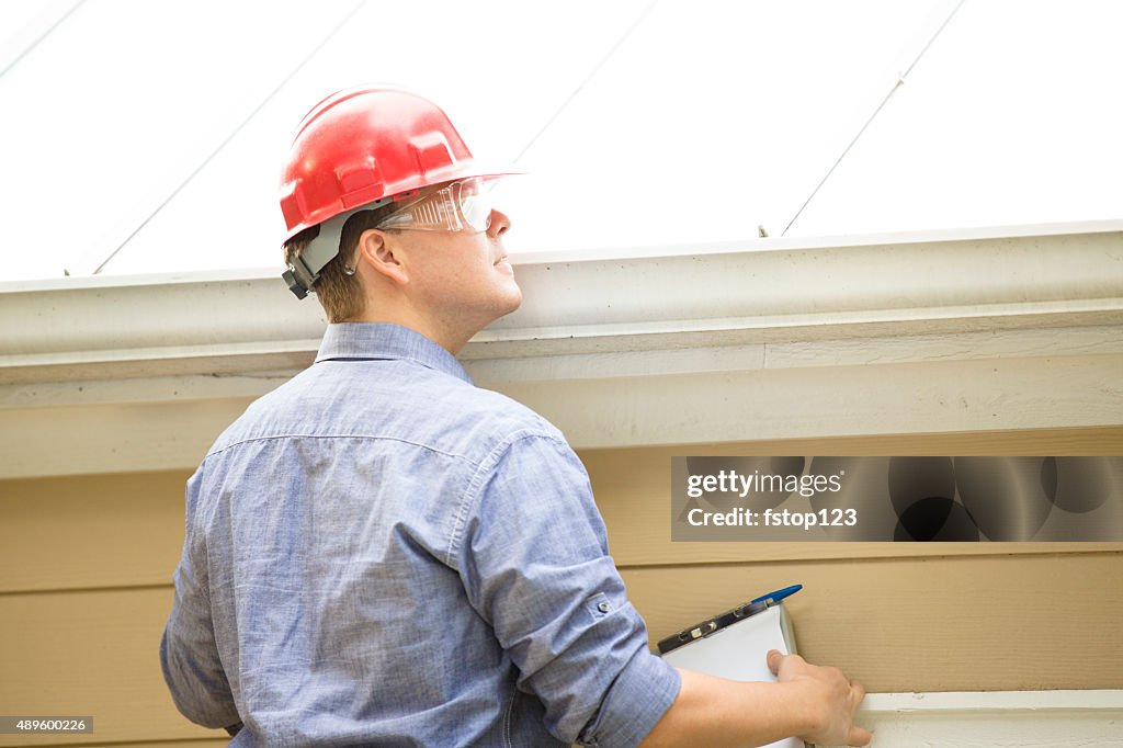 Inspector or blue collar worker examines building roof.  Outdoors.