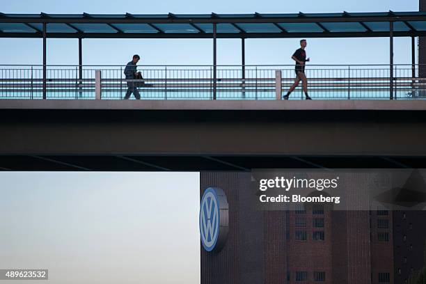 Pedestrian and a jogger pass along a covered external walkway as the Volkswagen AG headquarters stands beyond in Wolfsburg, Germany, on Wednesday,...