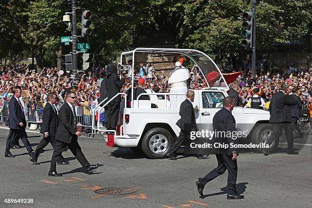 Surrounded by dozens of police cars and hundreds of security agents, Pope Francis waves to the crowd as he rides in a popemobile along a parade route...
