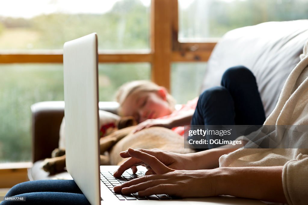 Mother using laptop whilst daughter sleeps