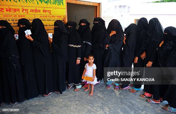 Child looks on as Indian Muslim women wait in line to cast their votes at a polling station in Azamgarh, about 275 kms from Lucknow in northern Uttar...