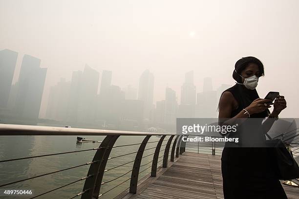 Pedestrian wearing a face mask uses a smart device at Marina Bay as buildings in the central business district stand shrouded in smog in Singapore,...