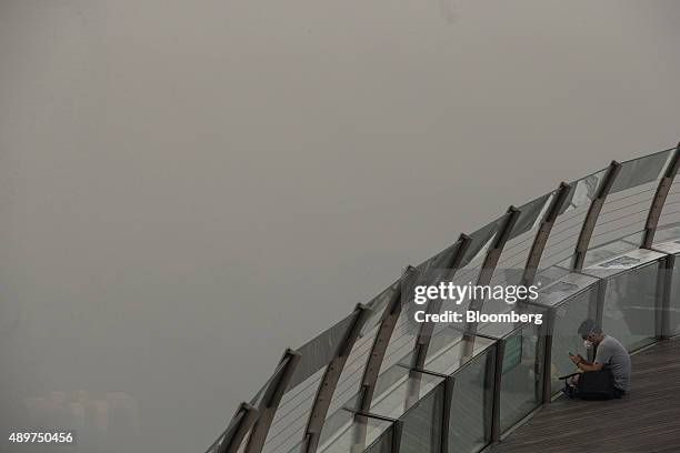 Pedestrian looks at a smart device from a viewing point in the Marina Bay district as buildings in the central business area stand shrouded in smog...