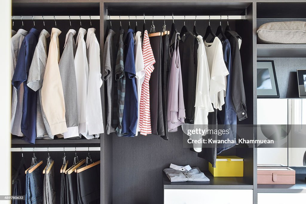 Modern closet with row of cloths hanging in black wardrobe