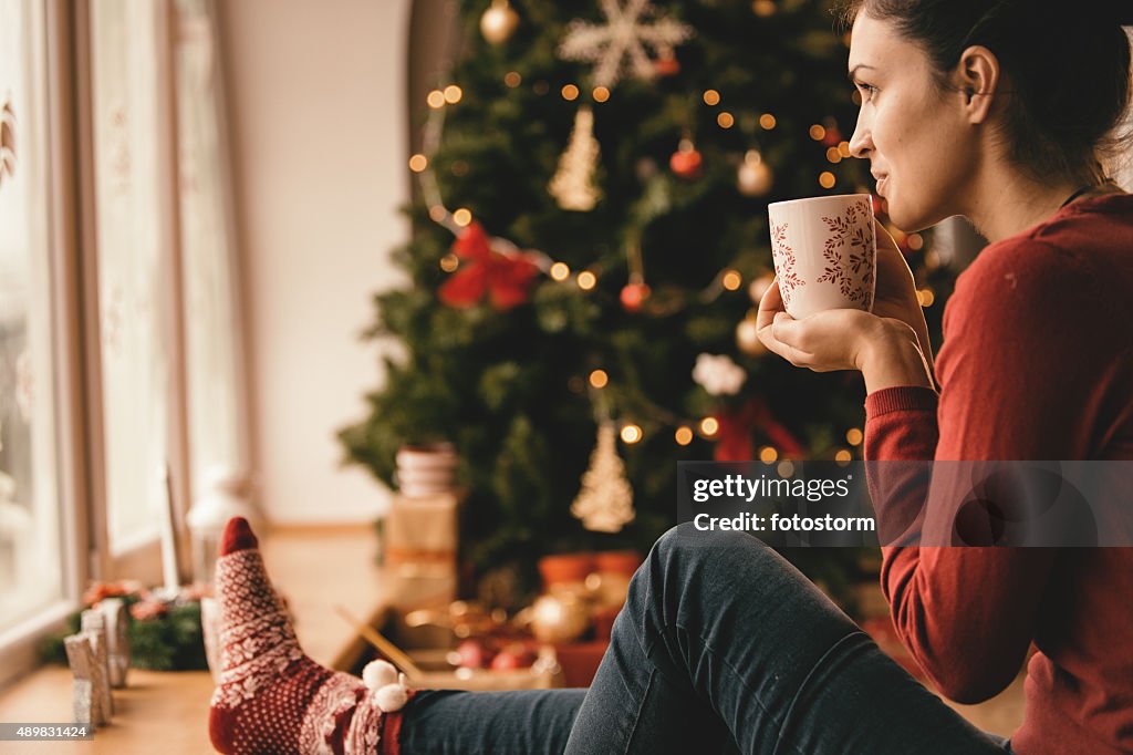 Young woman drinking tea by the Christmas tree