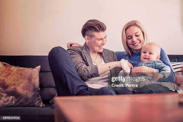 happy mothers playing with baby on sofa at home - cute lesbian couples stockfoto's en -beelden