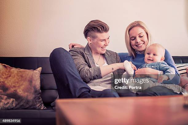 happy mothers playing with baby on sofa at home - cute lesbian couples 個照片及圖片檔