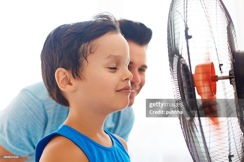 Boy with his dad cooling in front of fan.