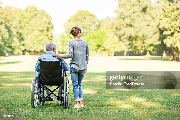 senior man sitting on a wheelchair with caregiver - social worker stockfoto's en -beelden