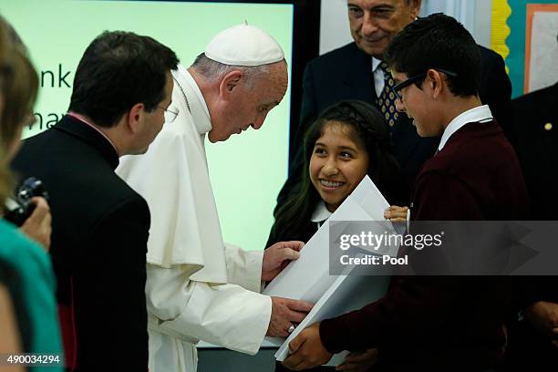 Pope Francis receives a book from Shaila Cuellar and Victor Franco during a visit to Our Lady Queen of Angels School September 21, 2015 in the East...