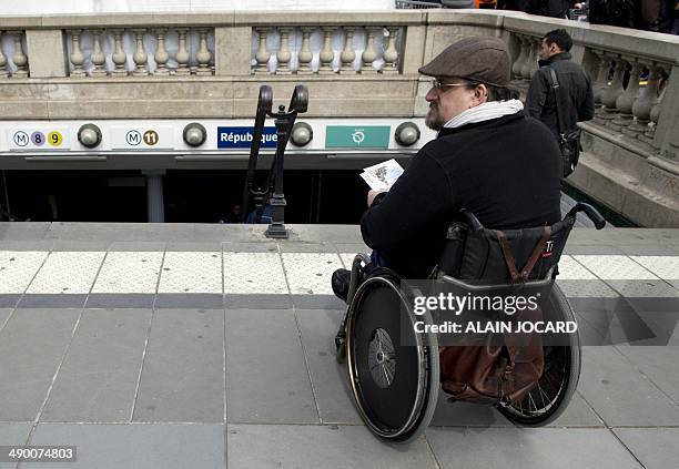 Disabled man in a wheelchair hands out flyers at the top of a metro station's stairs as he takes part in a demonstration called by the Paralysed...