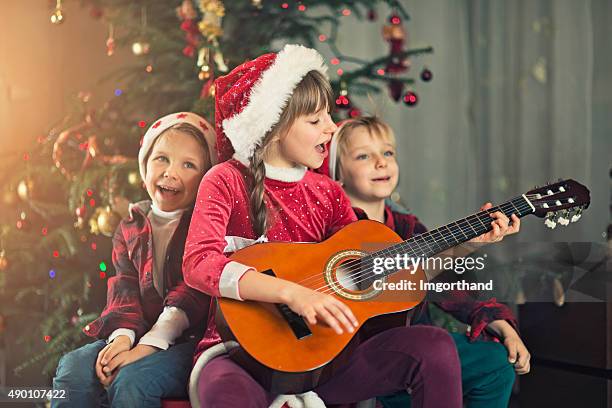 kinder singen carols in der nähe der weihnachtsbaum - christmas carols stock-fotos und bilder