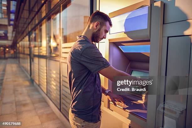 jeune homme d'affaires de retirer de l'argent à un distributeur automatique de billets. - dab photos et images de collection