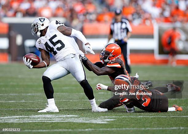 Marcel Reece of the Oakland Raiders avoids a tackle by Tashaun Gipson and Donte Whitner of the Cleveland Browns during the third quarter at...
