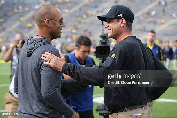 Head coach Jim Harbaugh of the Michigan Wolverines greets baseball great Derek Jeter of the New York Yankees on the sidelines prior to the game...