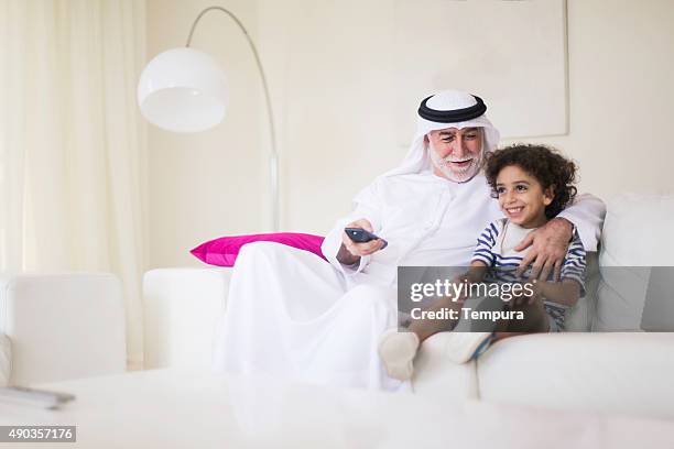 middle eastern grandfather watching tv at home with grandson. - arabian peninsula stock pictures, royalty-free photos & images
