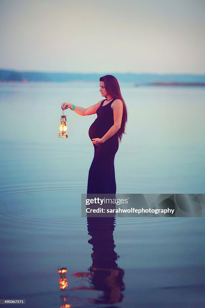 Pregnant woman standing in water with lantern