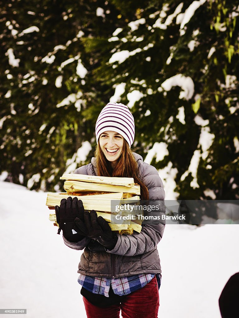 Smiling woman carrying firewood in snowy forest