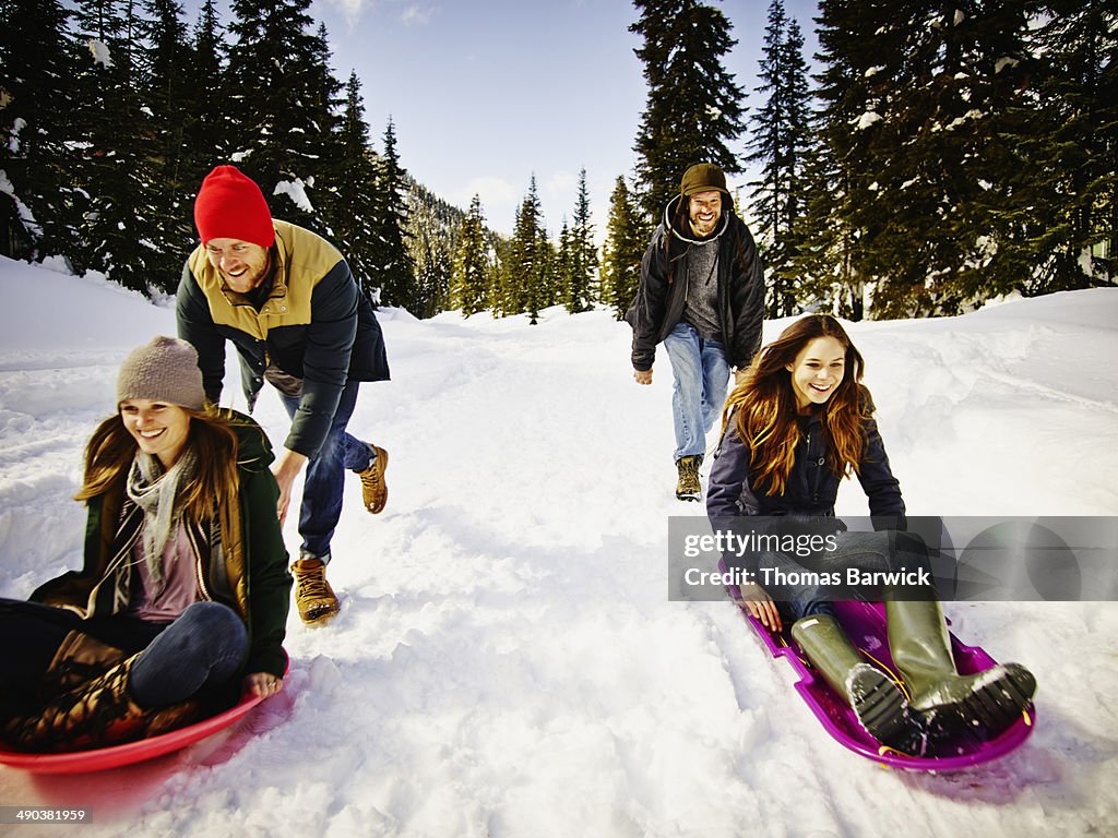 Smiling couples sledding down snowy road in forest