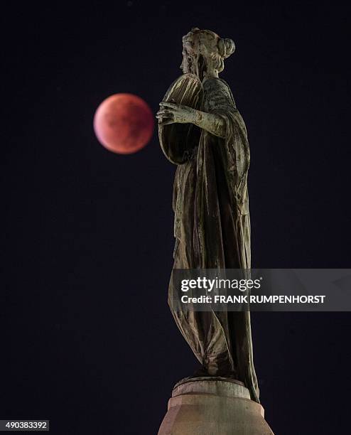 So-called "blood moon" can be seen behind a statue during a total lunar eclipse in Frankfurt am Main, western Germany, on September 28, 2015....