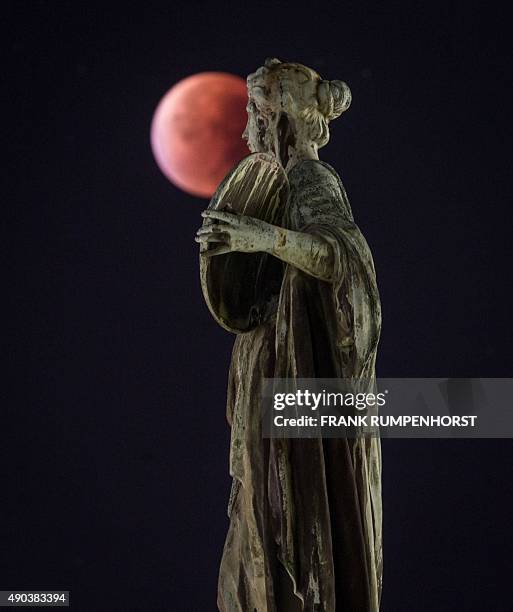 So-called "blood moon" can be seen behind a statue during a total lunar eclipse in Frankfurt am Main, western Germany, on September 28, 2015....
