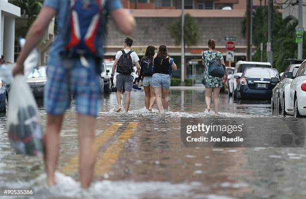 People walk through a flooded street that was caused by the combination of the lunar orbit which caused seasonal high tides and what many believe is...