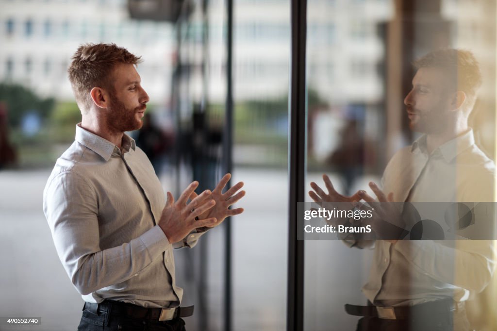 Smiling businessman talking to his reflection in window display.