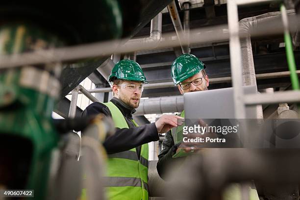 manual workers discussing while using laptop at factory - industrie stockfoto's en -beelden