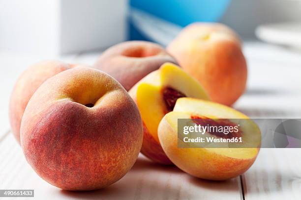 whole and sliced peaches (prunus persica) on white wooden table - peach half stock pictures, royalty-free photos & images