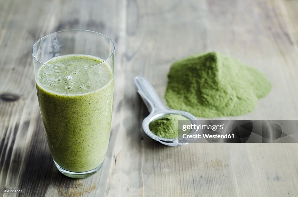 Moringa powder on spoon and wooden table and glass of moringa smoothie