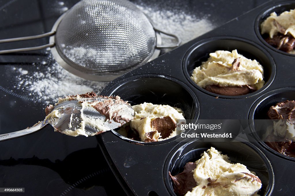 Raw muffin dough in muffin tray, spoon and strainer, close-up