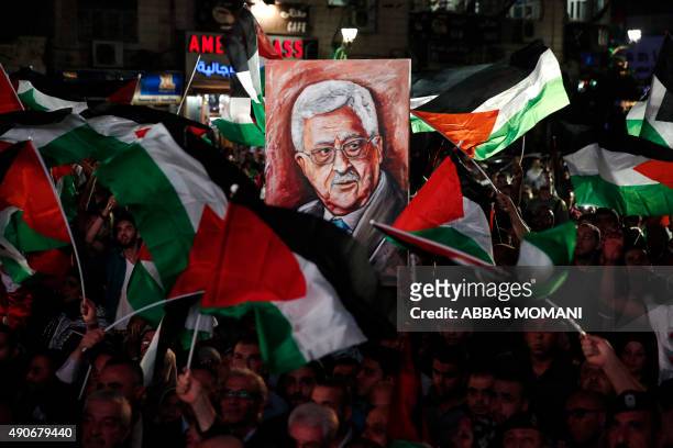 Palestinians wave their national flags and a portrait of their president Mahmud Abbas as they watch a live-screening of his speech followed by the...