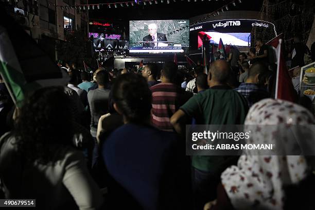 Palestinians wave their national flags as they watch a live-screening of president Mahmud Abbas' speech followed by the raising of the Palestinian...