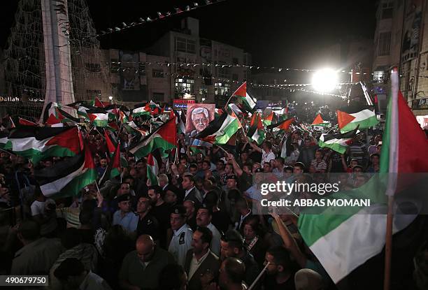 Palestinians wave their national flags as they watch a live-screening of president Mahmud Abbas' speech followed by the raising of the Palestinian...