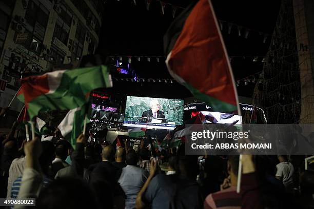 Palestinians wave their national flags as they watch a live-screening of president Mahmud Abbas' speech followed by the raising of the Palestinian...