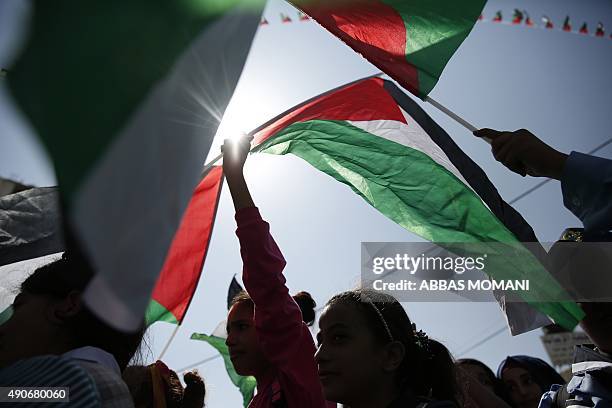 Palestinians wave their national flags as they watch a live-screening of president Mahmud Abbas' speech followed by the raising of the Palestinian...