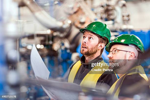 male colleagues analysing machine in industry - factory workers stockfoto's en -beelden