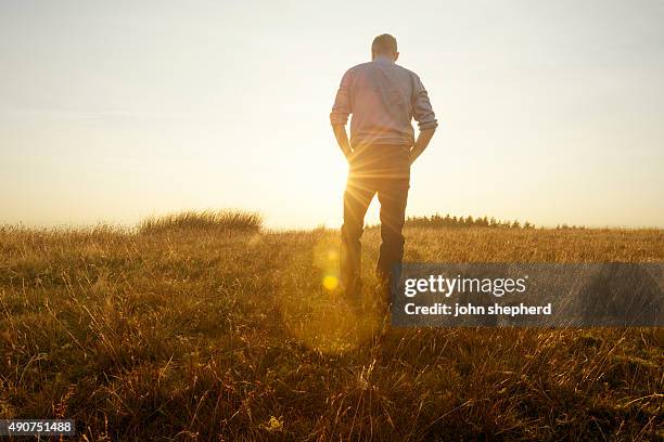 man walking in the countryside looking at the sunset - geting away from it all stock pictures, royalty-free photos & images