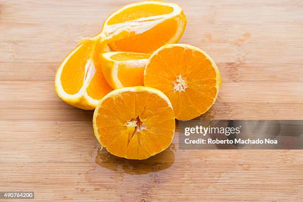 Pieces of orange fruit on a wooden chopping board. Two orange pieces are peeled and cut into half while the other pieces are quarter cut and unpeeled.