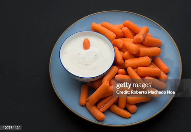 Baby carrots and a bowl full of delicious ranch sauce placed in a blue plate against a black background.