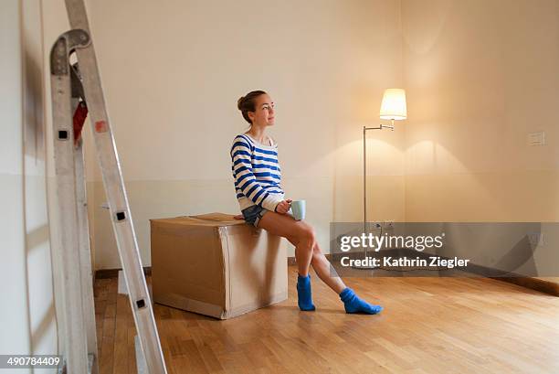 woman sitting on a box in her new, empty apartment - mudar de casa - fotografias e filmes do acervo