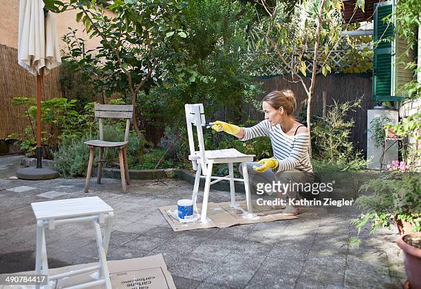woman painting wooden chairs in garden - garden furniture foto e immagini stock