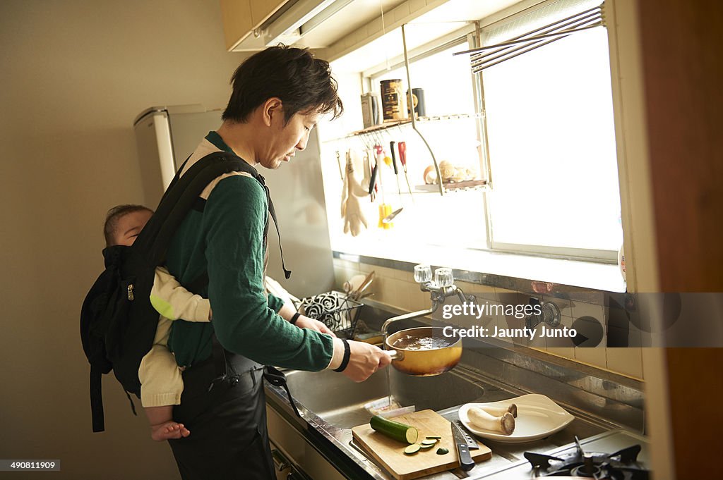 Father cooking and carrying his baby on his back.