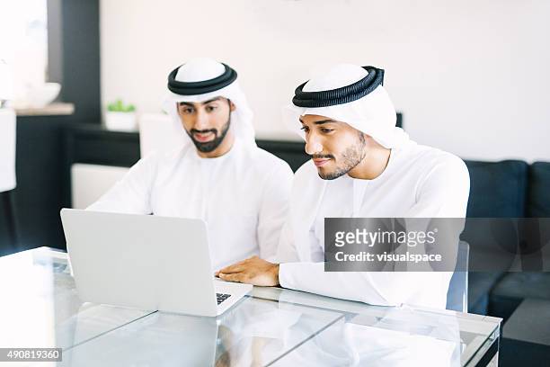 zwei arabische freunden sehen sie sich videos auf laptop - emirati guy using laptop stock-fotos und bilder